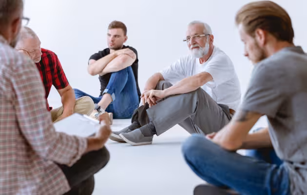 Grupo de hombres en sesión de terapia grupal, sentados en círculo durante su proceso de recuperación por adicciones